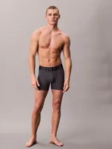 Pack de tres boxers largos Calvin Klein de microfibra, con talle medio y cinturilla elástica distintiva con el logo de la marca. Incluye un bóxer negro con elástico negro y letras blancas, un bóxer gris con elástico negro y letras grises, y un bóxer azul con elástico negro y letras azules.