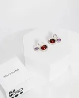 Aros abridores de plata con diseño asimétrico orgánico, incrustación de piedra roja principal y piedra morada pequeña.