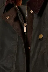 Chaqueta encerada de corte oversize, color marrón oscuro, con cuello de pana en contraste. Presenta cierre frontal con cremallera y botones a presión ocultos bajo solapa, bolsillos delanteros y mangas largas con puños ajustables.