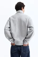 Buzo gris melange de tejido pesado de algodón con hombros caídos y cuello elevado con medio cierre. Presenta puños y bajo en punto acanalado, con el texto 'Golden' bordado en color bordó en el pecho.