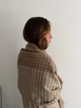 Bufanda de tejido suave con diseño de cuadros grandes en tonos negro y beige, terminada con flecos en los extremos.