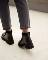 Bota corta de cuero color negro, estilo botín, con suela track gruesa y dos tiras ajustables con hebillas brillantes en el empeine.