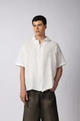 Camisa de manga corta confeccionada en lino, de corte relajado y cuello clásico. Presenta un diseño minimalista en color blanco con textura natural.