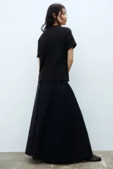 Remera negra de punto de algodón, de corte holgado con hombros caídos, cuello redondo acanalado y mangas cortas. Presenta dos apliques decorativos circulares de crochet en tono crudo a la altura del pecho.