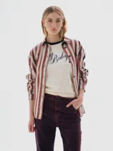 Camisa de denim con estampado de rayas verticales en tonos bordó y crema. Presenta cuello clásico, cierre frontal con botones negros, canesú trasero negro y paneles laterales negros en las mangas. Incluye un pequeño bordado con el nombre de la marca en el pecho.