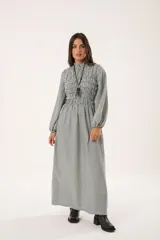 Vestido largo a rayas verticales en tonos verde y blanco, con cuello alto fruncido, mangas largas abullonadas y falda amplia. Presenta un diseño de nido de abeja con hilo elástico hasta la cintura.