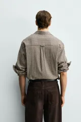 Camisa de corte relajado confeccionada en tejido de algodón con textura irregular y estampado de cuadros pequeños en tonos tierra. Presenta cuello solapa, cierre frontal de botones y mangas largas con puños abotonados.