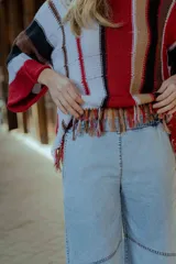 Sweater tejido en hilado 100% algodón con diseño a rayas verticales en tonos rojo, blanco, marrón y negro. Presenta flecos en el ruedo y bordados en el escote.