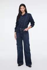 Enterito largo confeccionado en denim azul, con cuello camisero, cierre frontal con botones, mangas largas, cinturón incorporado con hebilla metálica, bolsillos aplicados en el pecho y bolsillos estilo cargo en los laterales de las piernas.
