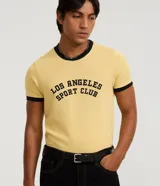 Remera tipo baby tee de color amarillo con ribetes negros en el cuello redondo y los puños de las mangas cortas. Cuenta con una estampa central en el pecho con la inscripción "Los Angeles Sport Club" en color negro.