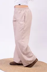 Pantalón de pierna ancha y tiro alto color beige, confeccionado en tela con textura ligera, con cintura elástica y bolsillos laterales.