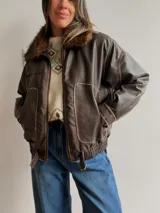 Campera estilo bomber de efecto cuero en color chocolate, con cuello de pelo sintético desmontable, cierre frontal, bolsillos laterales amplios y cintura elástica con ajuste lateral.