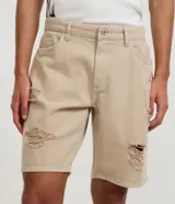Bermuda masculina de sarga color beige, corte slim, con diseño destroyed que incluye rotos y efecto desgastado. Cuenta con cintura fija con trabillas, cierre de botón y cremallera, y bolsillos laterales y traseros.