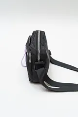 Cartera tipo bandolera de nylon color lila, con cierre frontal y correa ajustable negra.