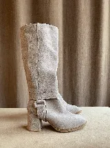 Botas de caña alta desmontables que se transforman en botinetas, confeccionadas en gamuza color beige. Presentan un diseño de punta semicuaadrada, taco cuadrado de 6 cm y detalle de estribo con hebilla forrada en el tobillo.