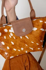 Cartera tipo bolso de mano confeccionada en cuero gamuzado color suela, con solapa de cuero liso y cierre metálico. Incluye doble manija corta y correa larga desmontable.