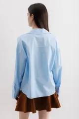 Camisa blanca de algodón, de corte holgado, con cuello clásico, mangas largas con puños anchos y un bolsillo de parche en el lateral.