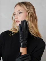 Guantes de cuero sintético color negro, con costuras decorativas en el dorso y detalle de tira con broche a presión en la muñeca. Interior forrado en terciopelo.