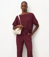 Pantalón de crepé rojo, modelo estilo pijama, de corte fluido, con cintura elástica y lazo de ajuste con terminales metálicas. Cuenta con bolsillos laterales y cierre frontal con cremallera y botón.