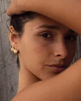 Aros pequeños de bronce con forma irregular y acabado liso, estilo huggie o argolla gruesa.