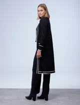 Cardigan largo tejido de punto color negro con detalles de líneas blancas en los bordes delanteros, puños y bolsillos. Cuenta con mangas largas y bolsillos frontales aplicados con botones decorativos dorados.