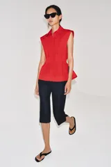 Camisa de cuello solapa y manga sisa, de color blanco. Presenta bajo acabado en peplum y cierre frontal con botones ocultos.