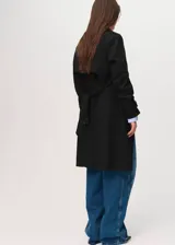 Abrigo tipo trench color negro, de diseño recto y cruzado con cierre de botones. Cuenta con cuello de solapa, mangas largas con trabillas en los puños, cinturón ajustable y dos bolsillos laterales.