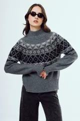 Sweater de punto color marrón, con cuello alto y diseño tejido con patrones geométricos en tonos negros y blancos en la parte superior y mangas.