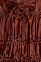 Blusa marrón de lyocell con escote redondo, mangas cortas abullonadas y cuerpo fruncido con detalle de tiras decorativas.