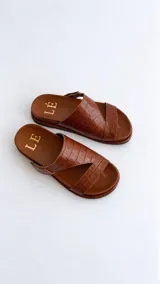 Sandalias de cuero color marrón con diseño asimétrico de tiras y plantilla anatómica. Tienen ajuste lateral con velcro y suela plana.