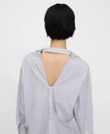 Camisa de algodón a rayas blancas y azules con diseño desestructurado, cuello italiano, manga larga y cierre de botones. Cuenta con una pieza asimétrica multiposición en la parte frontal.