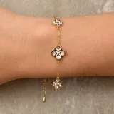 Pulsera de cadena fina dorada con tres dijes en forma de flor. El dije central presenta un diseño calado con incrustaciones de nácar y un pequeño cristal, mientras que los dos dijes laterales están completamente cubiertos de cristales brillantes.