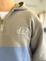 Hoodie de felpa con capucha y medio cierre frontal, diseño en bloques de color celeste y blanco, con bordados decorativos en el pecho.