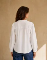 Camisa blanca de manga larga con detalles de encaje, pliegues frontales y cuello con volados.
