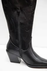 Bota texana de caña alta, confeccionada en material símil gamuza con terminación suave. Presenta diseño bordado sobre la caña, punta fina y taco medio ancho.
