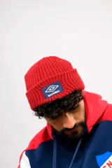 Gorro de lana Umbro color rojo con vuelta, tejido en canalé, con parche frontal azul que incluye el logo de Umbro y la inscripción "Nacional".
