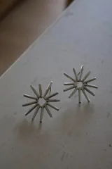 Par de aros plateados con forma de sol, con centro circular y rayos cilíndricos.