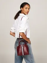 Cartera tote Tommy Hilfiger color borgoña, con doble asa corta y correa larga extraíble. Presenta una franja vertical con los colores de la marca y el logo TH dorado.