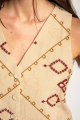 Chaleco de algodón color beige con estampado geométrico en tonos bordó y marrón. Presenta escote en V, cierre frontal con botones y corte recto.