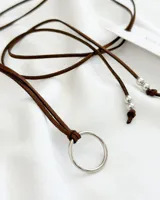 Gargantilla tipo choker con cordón de cuero marrón, dije circular plateado y cuentas plateadas.