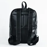 Mochila negra con diseño acolchado de hexágonos que simula la textura de una pelota de fútbol. Cuenta con un bolsillo frontal con cierre metálico y logo circular plateado en la parte inferior.