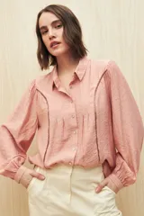 Camisa blanca de manga larga con cuello clásico y botones de nácar. Presenta detalles calados en el frente.