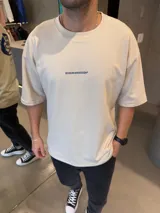 Remera oversize de algodón pesado en color beige, con estampa gráfica en azul en la espalda que incluye texto y un trazo circular.