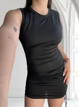 Vestido corto negro ajustado al cuerpo, sin mangas y con frunces laterales.