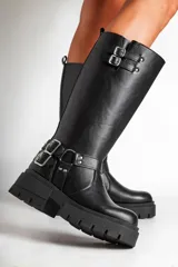 Borcegos negros de ecocuero con caña alta y base con plataforma. Presentan correas con hebillas plateadas en la parte superior y alrededor del tobillo.