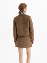 Chaqueta matelaseada color marrón, de corte recto y largo a la cadera, con cuello redondo, cierre frontal con broches dorados y bolsillos plaqué en el delantero.