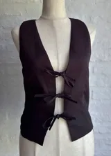 Chaleco negro con escote en V profundo y cierre frontal mediante lazos ajustables.