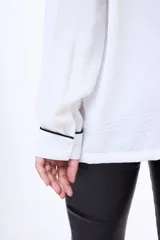 Camisa negra de manga larga con cuello estilo pijama y cierre frontal de botones. Presenta un vivo blanco en contraste que recorre el cuello, la tapeta de botones y los puños.