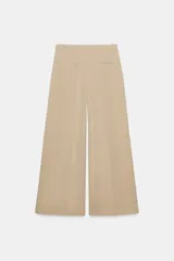 Pantalón de tiro medio con corte wide leg, confeccionado en algodón. Presenta cintura con trabillas, bolsillos laterales ocultos y detalle de pliegues en el delantero. Cierre frontal con cremallera, botón y ganchos metálicos.
