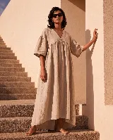 Vestido largo amplio de lino natural, color beige, con escote en V, costura fruncida bajo el busto y mangas cortas holgadas.